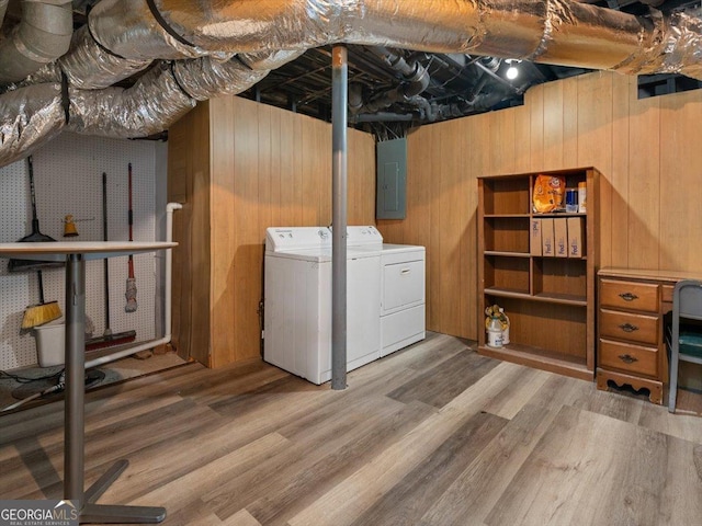 laundry area featuring electric panel, washing machine and dryer, hardwood / wood-style flooring, and wood walls