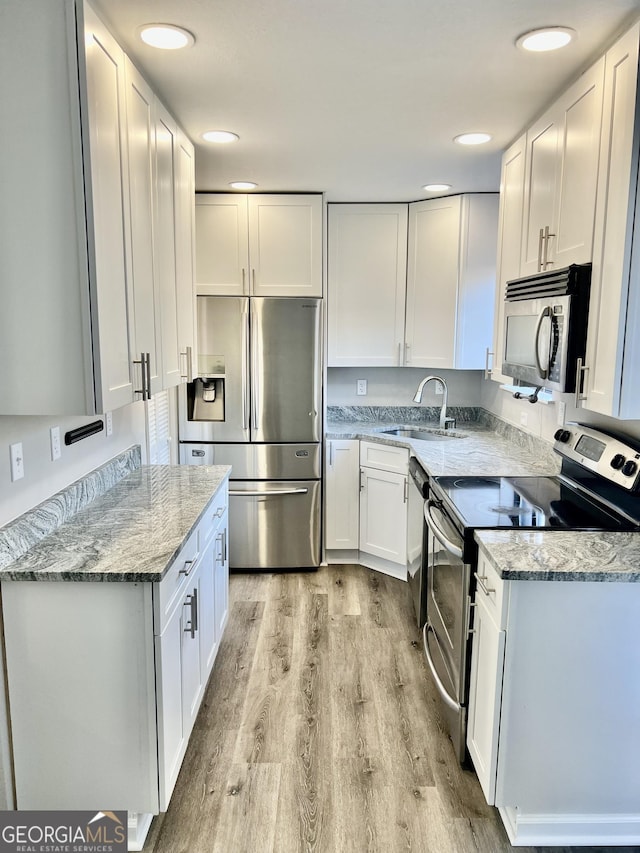 kitchen with light stone countertops, white cabinetry, sink, and stainless steel appliances