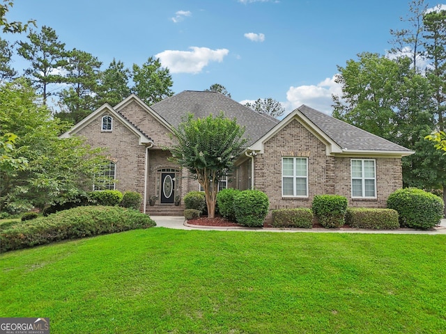 view of front facade with brick siding, a front lawn, and roof with shingles