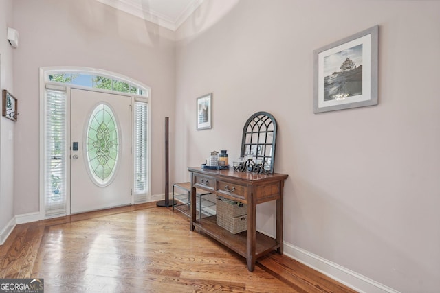 foyer with ornamental molding, a towering ceiling, baseboards, and wood finished floors