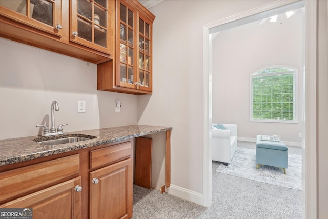 kitchen with glass insert cabinets, light carpet, a sink, dark stone countertops, and baseboards