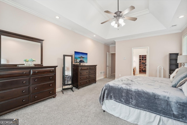 bedroom featuring a walk in closet, a raised ceiling, visible vents, ornamental molding, and light carpet