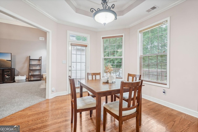 dining area with visible vents, baseboards, light wood finished floors, ornamental molding, and a tray ceiling