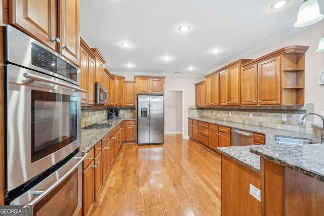 kitchen featuring stainless steel appliances, a sink, ornamental molding, brown cabinets, and dark stone countertops