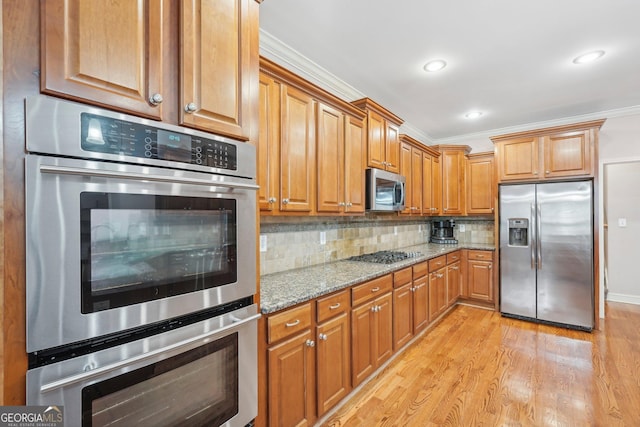 kitchen with light stone counters, brown cabinets, backsplash, appliances with stainless steel finishes, and light wood-style floors