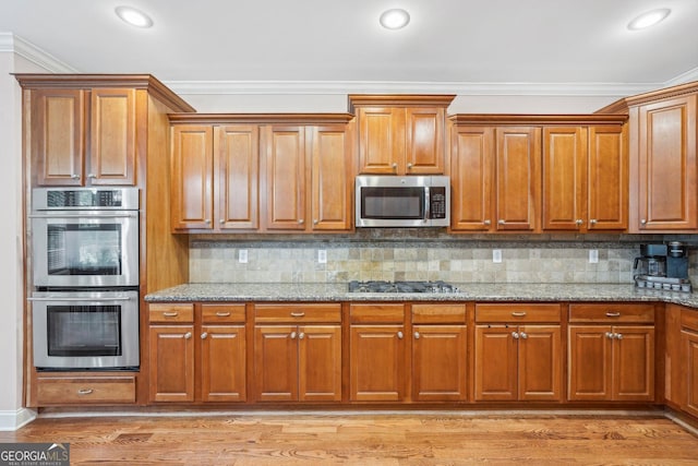 kitchen with light wood finished floors, light stone counters, brown cabinets, ornamental molding, and stainless steel appliances