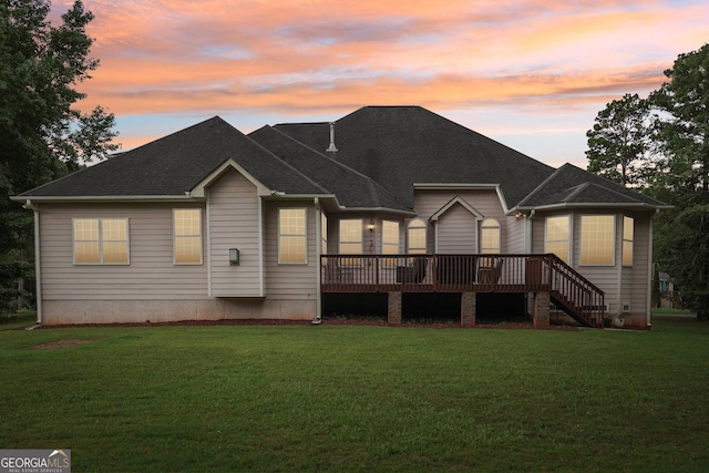 back of house at dusk with a yard, stairway, a wooden deck, and roof with shingles