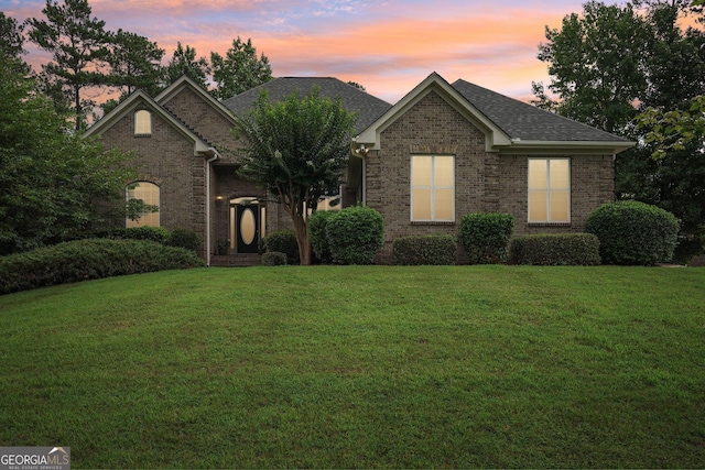 view of front of home with brick siding, a lawn, and roof with shingles