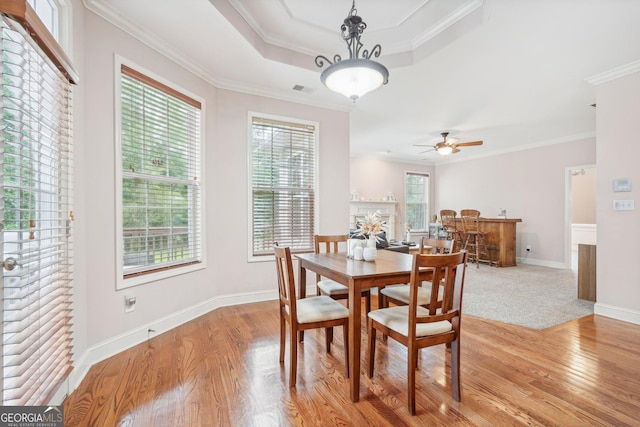 dining area with light wood-type flooring, baseboards, a tray ceiling, and crown molding