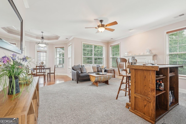 living area with wood finished floors, visible vents, baseboards, a raised ceiling, and crown molding