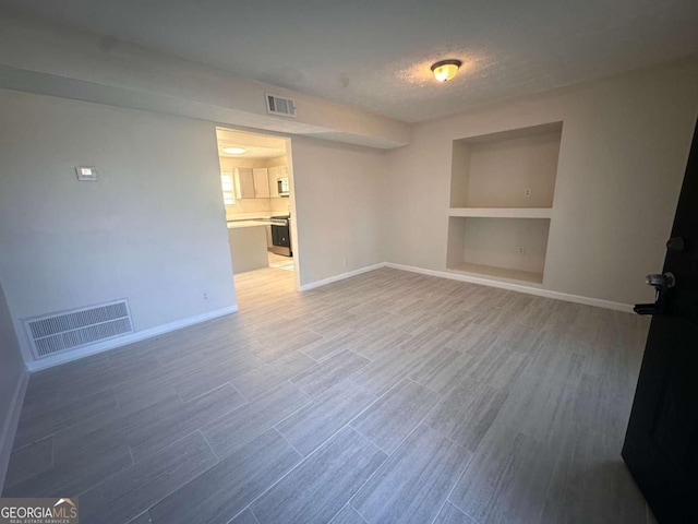 unfurnished room featuring built in shelves, a textured ceiling, and hardwood / wood-style flooring