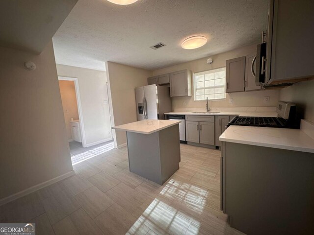 kitchen with gray cabinets, sink, a center island, and appliances with stainless steel finishes