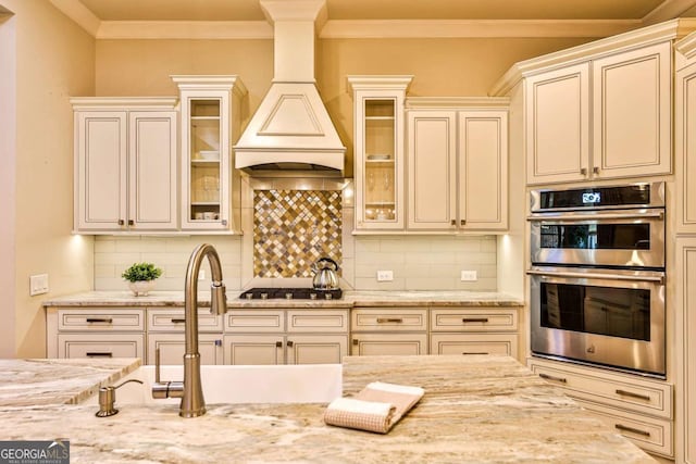 kitchen featuring light stone counters, decorative backsplash, stainless steel appliances, and custom range hood