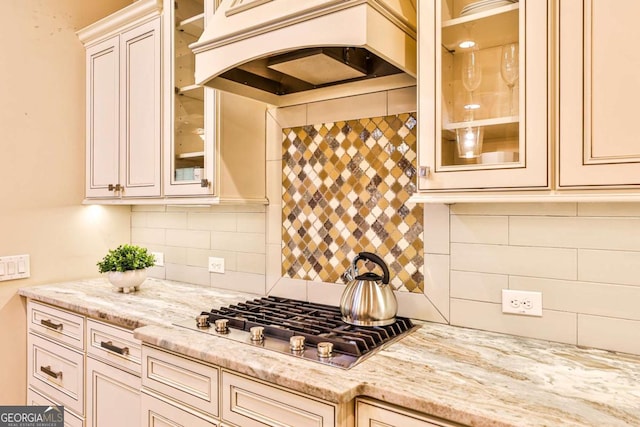 kitchen with stainless steel gas stovetop, custom exhaust hood, light stone counters, and tasteful backsplash