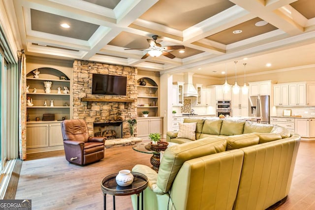 living room with light wood-type flooring, coffered ceiling, crown molding, beam ceiling, and a stone fireplace