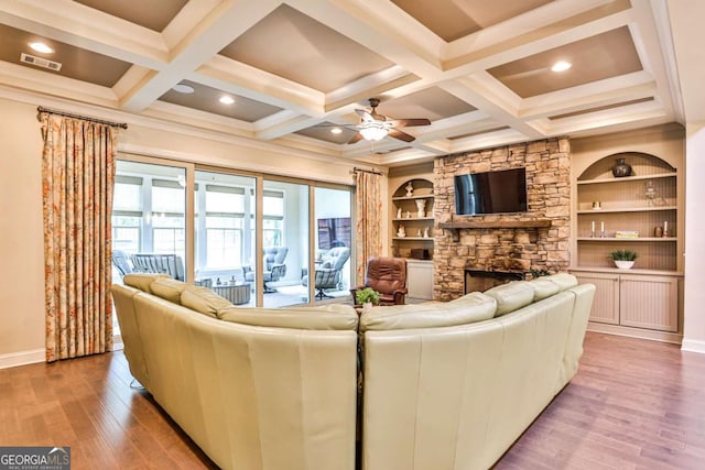 living room featuring built in shelves, a stone fireplace, ceiling fan, and wood-type flooring