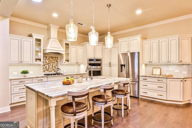 kitchen with light stone countertops, appliances with stainless steel finishes, a kitchen island with sink, hanging light fixtures, and a breakfast bar area