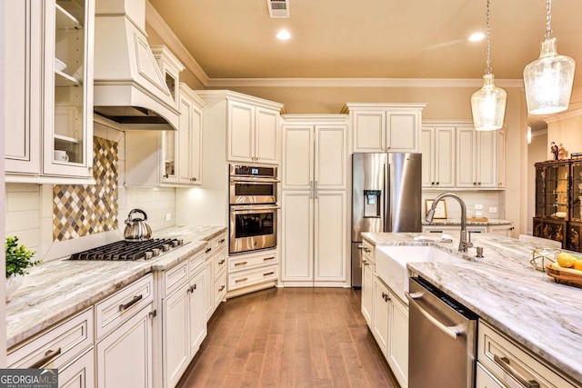 kitchen with decorative backsplash, appliances with stainless steel finishes, premium range hood, sink, and hanging light fixtures