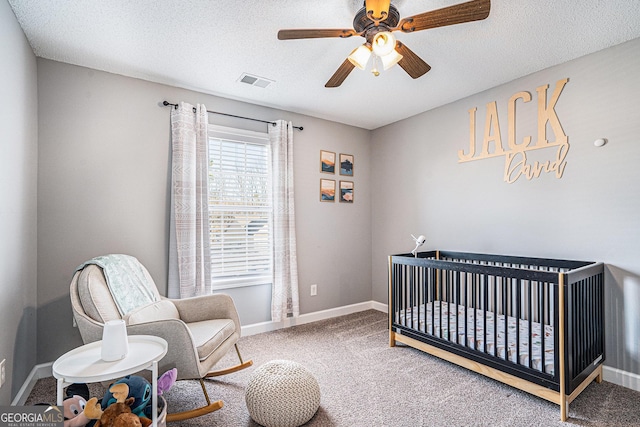 bedroom featuring a crib, a textured ceiling, carpet, and ceiling fan