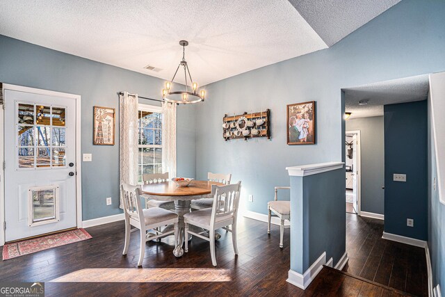 dining area with dark wood-type flooring, a textured ceiling, and a notable chandelier