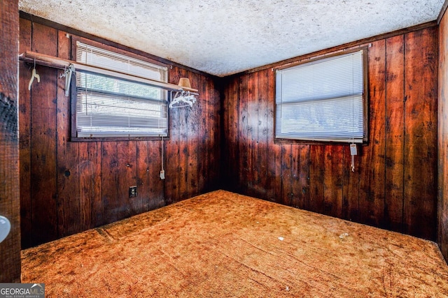 carpeted spare room featuring a textured ceiling and wooden walls