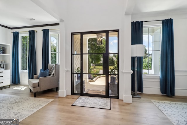 entryway featuring a wealth of natural light, ornamental molding, and light wood-type flooring