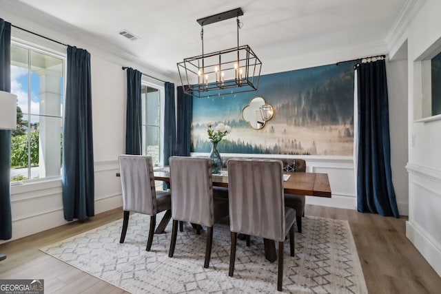 dining area featuring light wood-type flooring, ornamental molding, and a notable chandelier