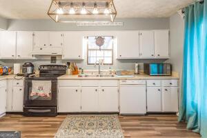 kitchen featuring black electric range, white dishwasher, light countertops, and white cabinets