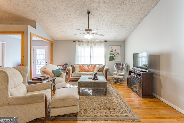 living room featuring a textured ceiling, light hardwood / wood-style floors, vaulted ceiling, and ceiling fan