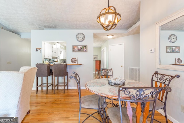 dining space featuring light hardwood / wood-style floors, a textured ceiling, and a chandelier