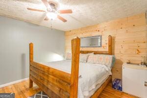 bedroom with ceiling fan, wood walls, and wood finished floors