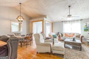 living area with light wood-style floors, a textured ceiling, vaulted ceiling, and a ceiling fan