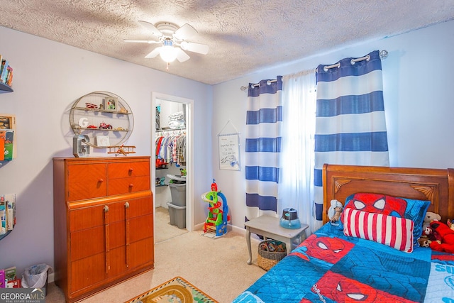 bedroom with a textured ceiling, light colored carpet, ceiling fan, a spacious closet, and a closet