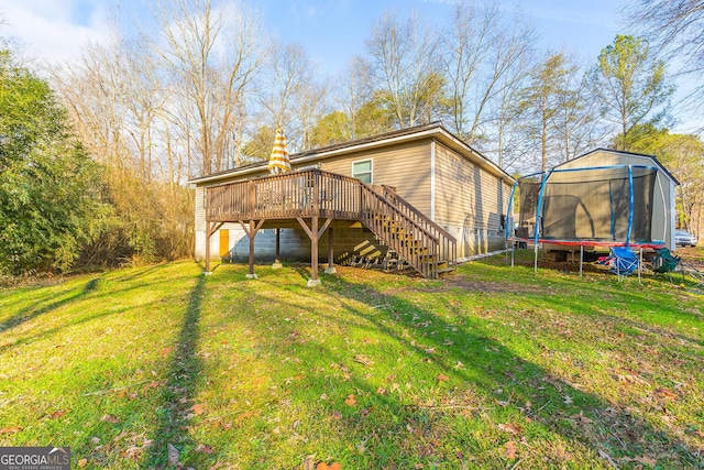 back of property with a trampoline, a deck, and a lawn