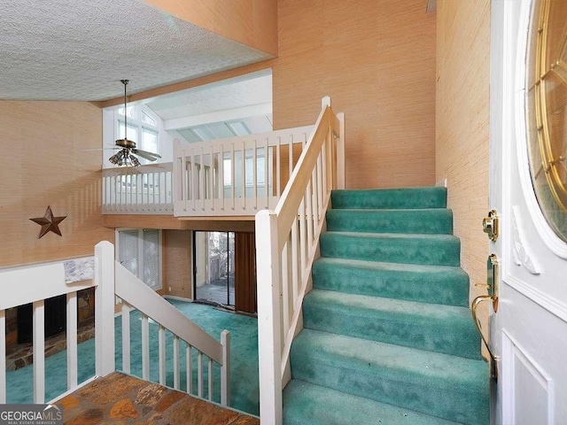 stairway featuring ceiling fan, carpet floors, a textured ceiling, and high vaulted ceiling