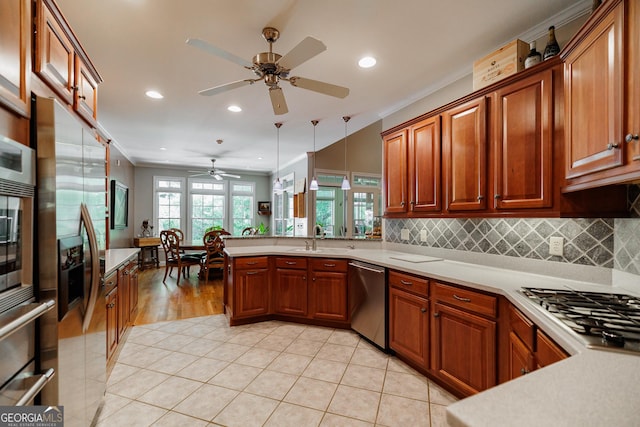 kitchen featuring kitchen peninsula, appliances with stainless steel finishes, ceiling fan, crown molding, and hanging light fixtures