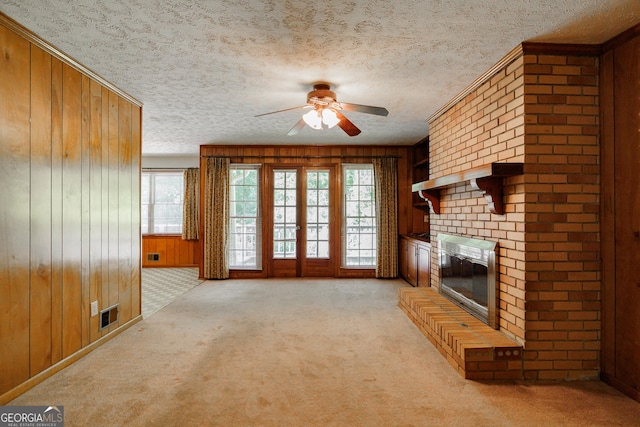 unfurnished living room with ceiling fan, wood walls, light colored carpet, a textured ceiling, and a fireplace