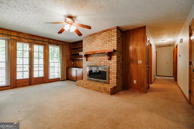 unfurnished living room featuring ceiling fan, wood walls, a textured ceiling, light carpet, and a fireplace