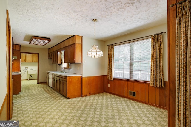 kitchen featuring wood walls, sink, pendant lighting, and a textured ceiling