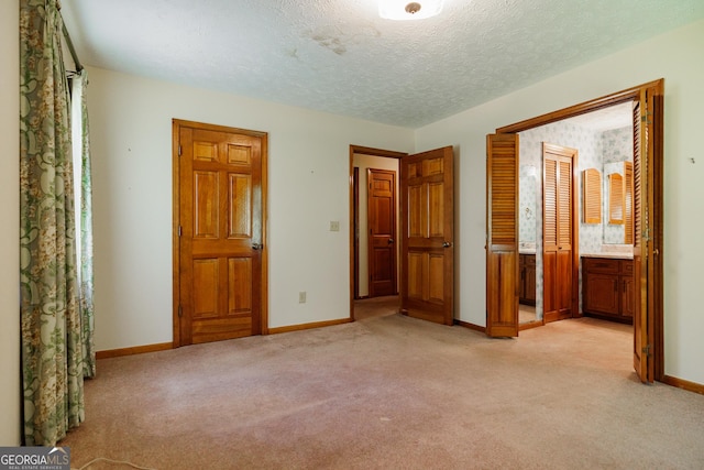 unfurnished bedroom featuring connected bathroom, light colored carpet, and a textured ceiling