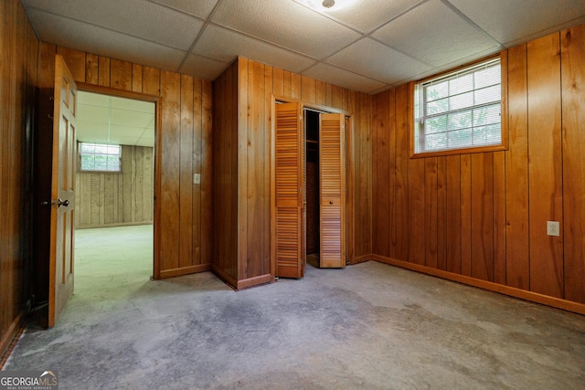 unfurnished bedroom featuring a paneled ceiling, wooden walls, and a closet