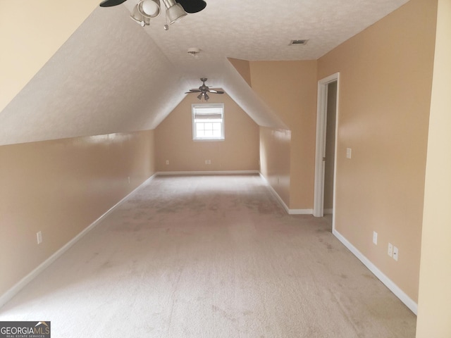 additional living space featuring vaulted ceiling, ceiling fan, light colored carpet, and a textured ceiling