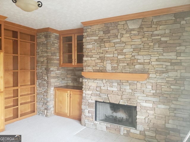 unfurnished living room featuring light carpet, built in shelves, a textured ceiling, and a stone fireplace