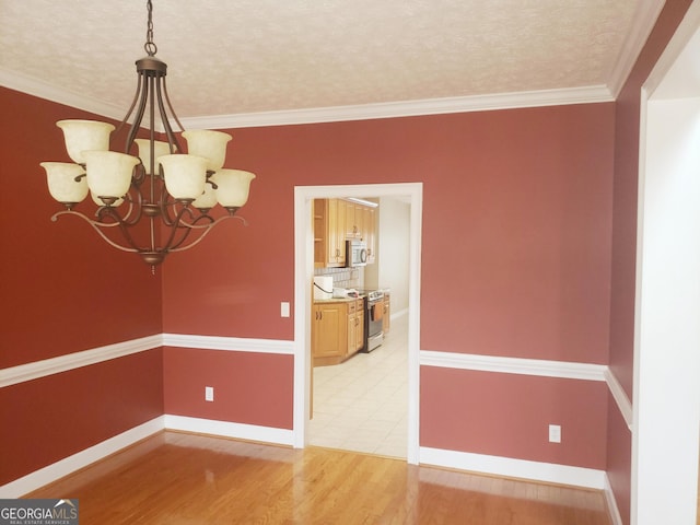 empty room with hardwood / wood-style floors, a textured ceiling, crown molding, and a notable chandelier