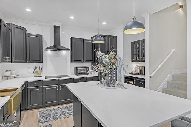 kitchen with light wood-type flooring, wall chimney exhaust hood, black electric cooktop, crown molding, and decorative light fixtures