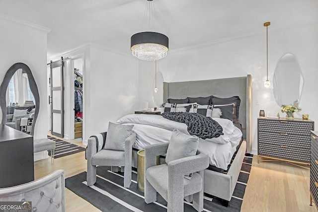 bedroom with a barn door, wood-type flooring, and ornamental molding