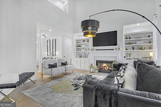 living room with built in shelves, hardwood / wood-style floors, and a towering ceiling