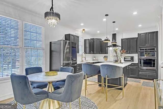 kitchen with island exhaust hood, light wood-type flooring, stainless steel appliances, decorative light fixtures, and a center island