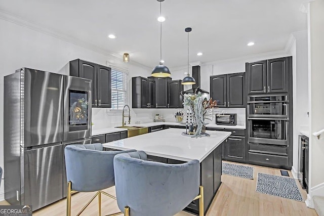 kitchen with sink, stainless steel appliances, light hardwood / wood-style floors, decorative light fixtures, and a kitchen island