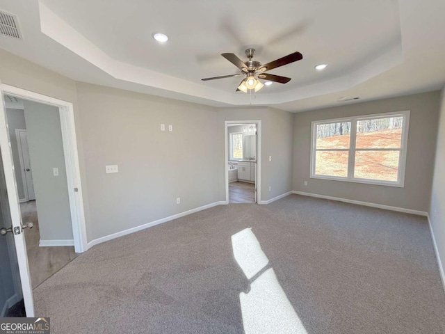 unfurnished bedroom featuring carpet, a tray ceiling, ensuite bath, and ceiling fan